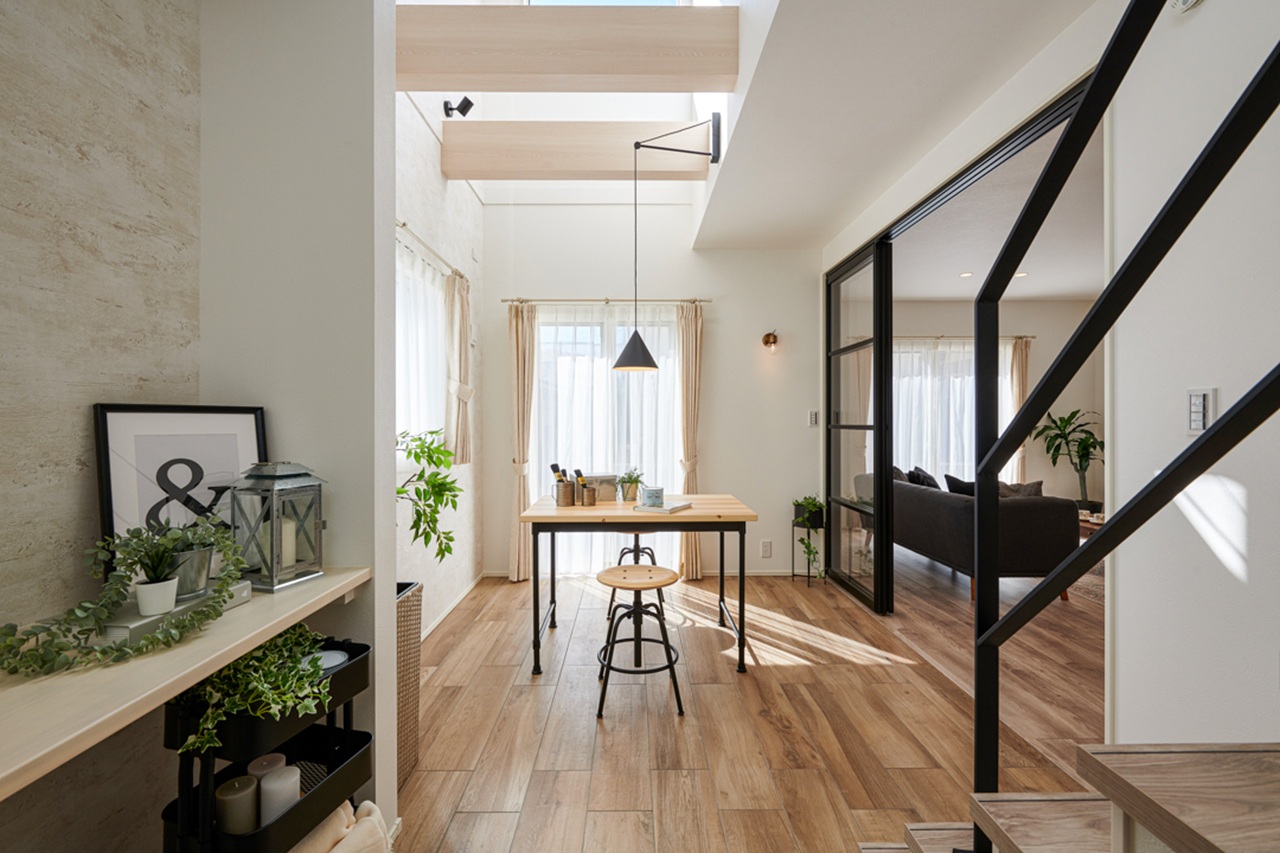 吹き抜けと階段のある明るいダイニングスペースに、木製テーブルが配置された住空間