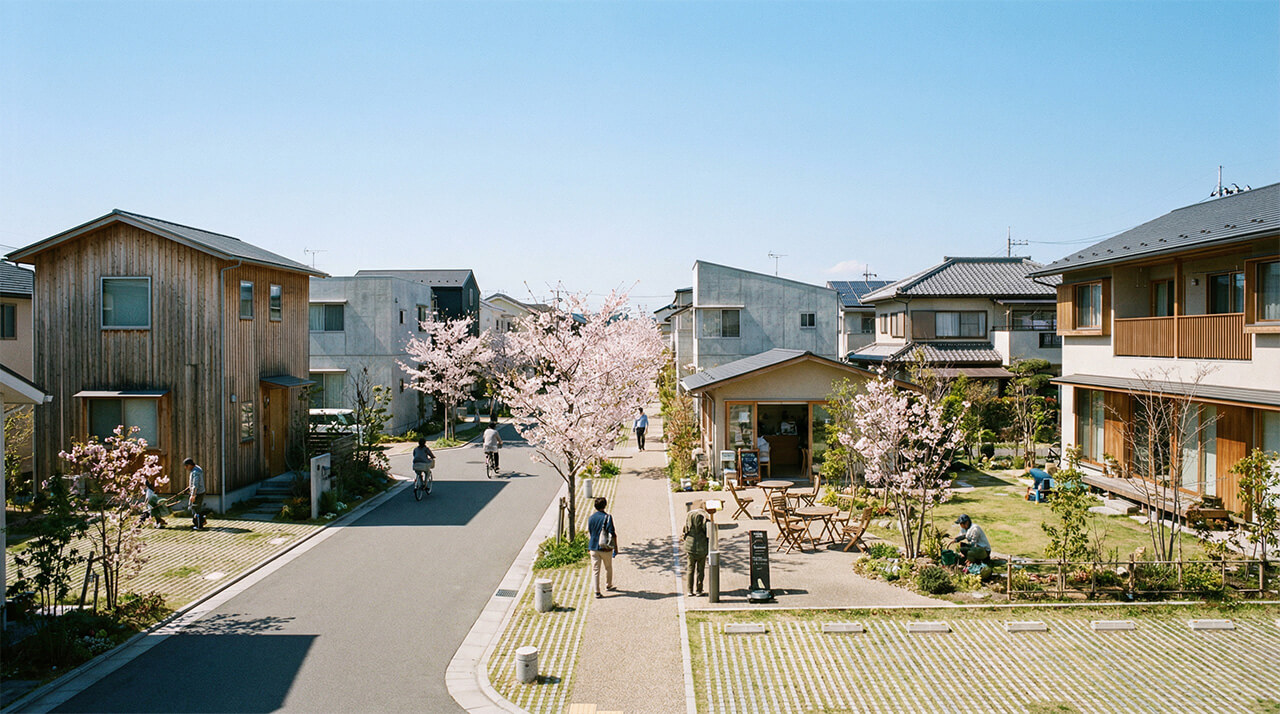 桜が咲く歩行者中心の住宅街で、人々が穏やかに行き交う様子