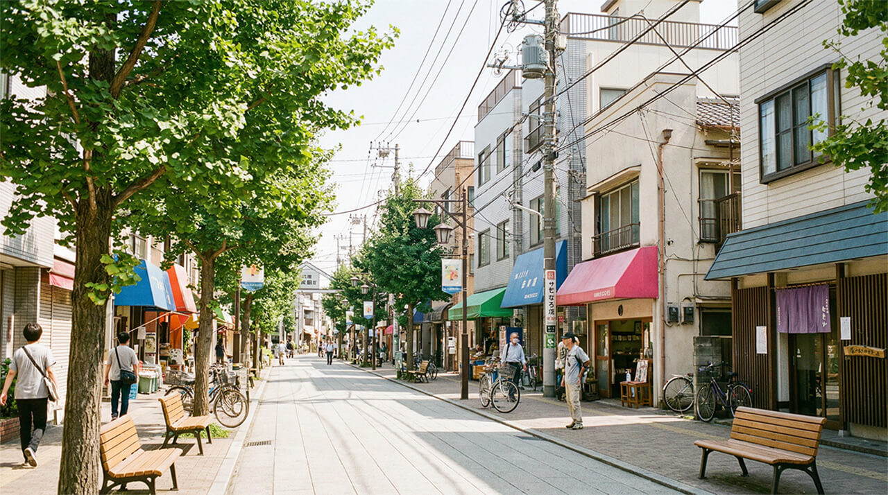 街路樹と商店が並び、歩行者が行き交う落ち着いた商店街の様子