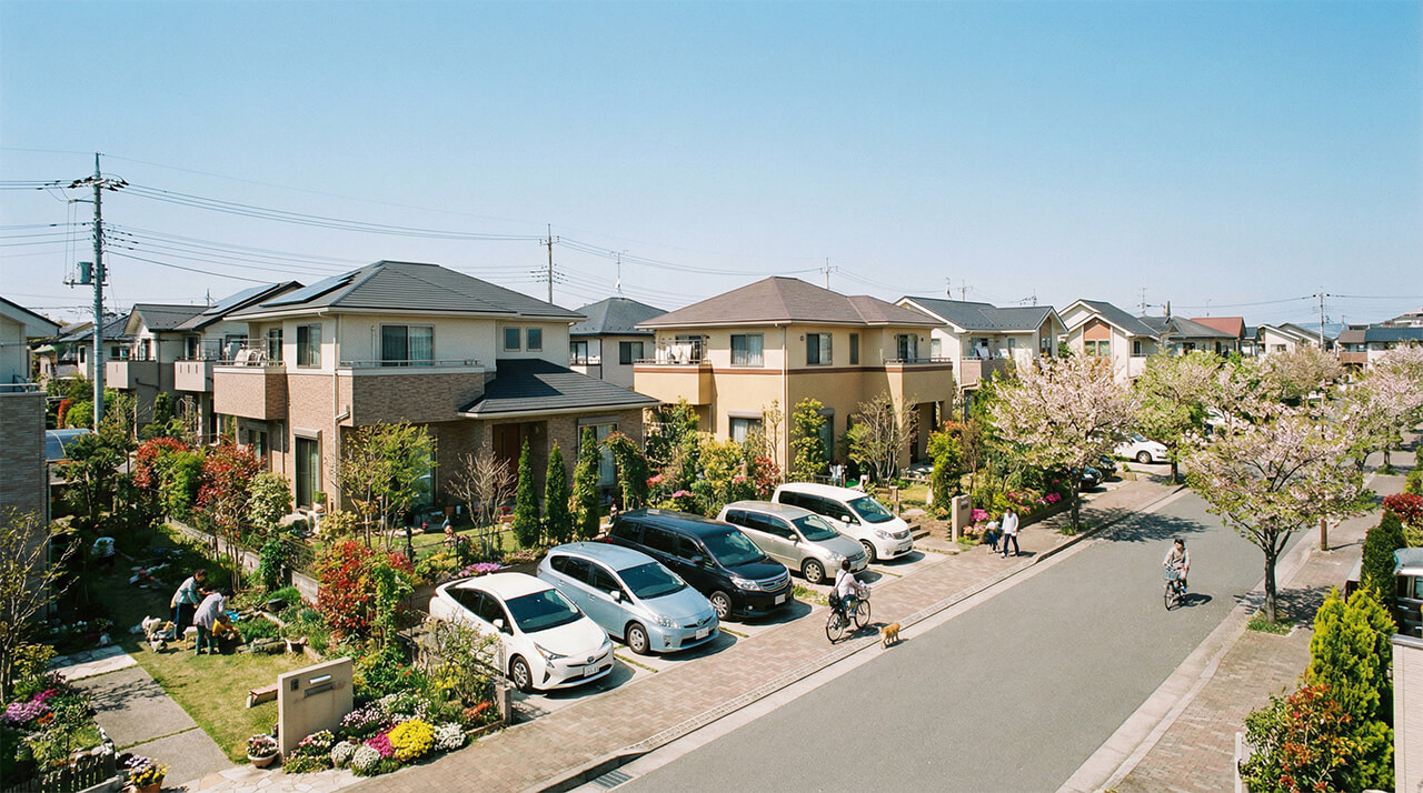 桜並木と庭付き住宅が広がり、住民が行き交う穏やかな住宅街の様子