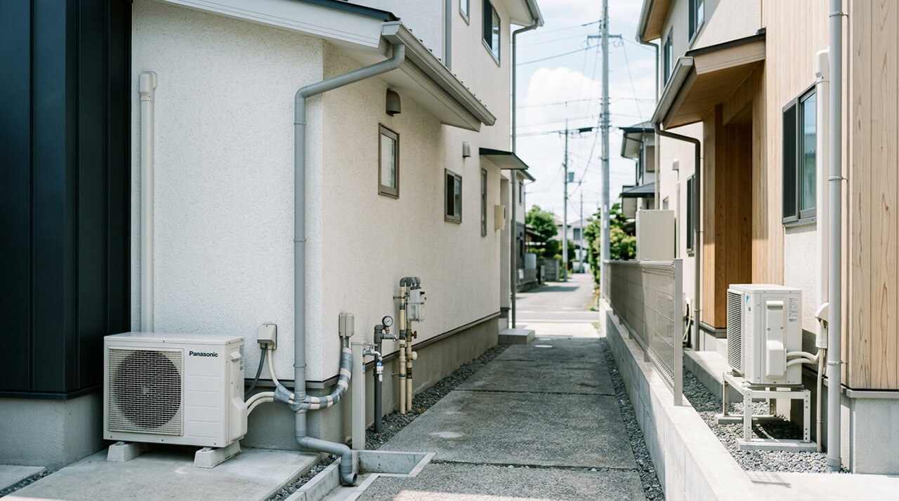 住宅の間の狭い通路に室外機や配管が設置された様子